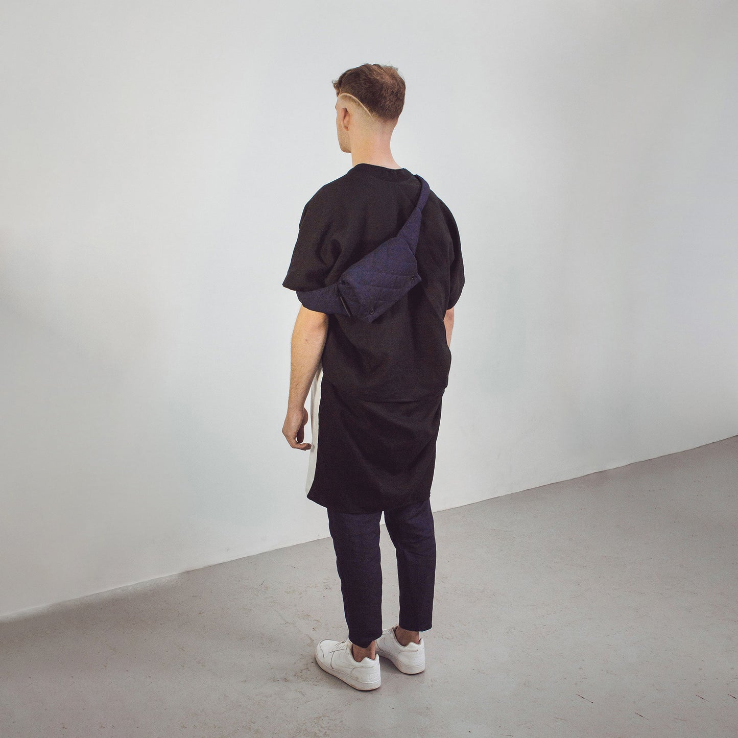 Back view of man wearing black and white Linen Cocoon Long Jacket with navy linen belt bag by The Costume Room