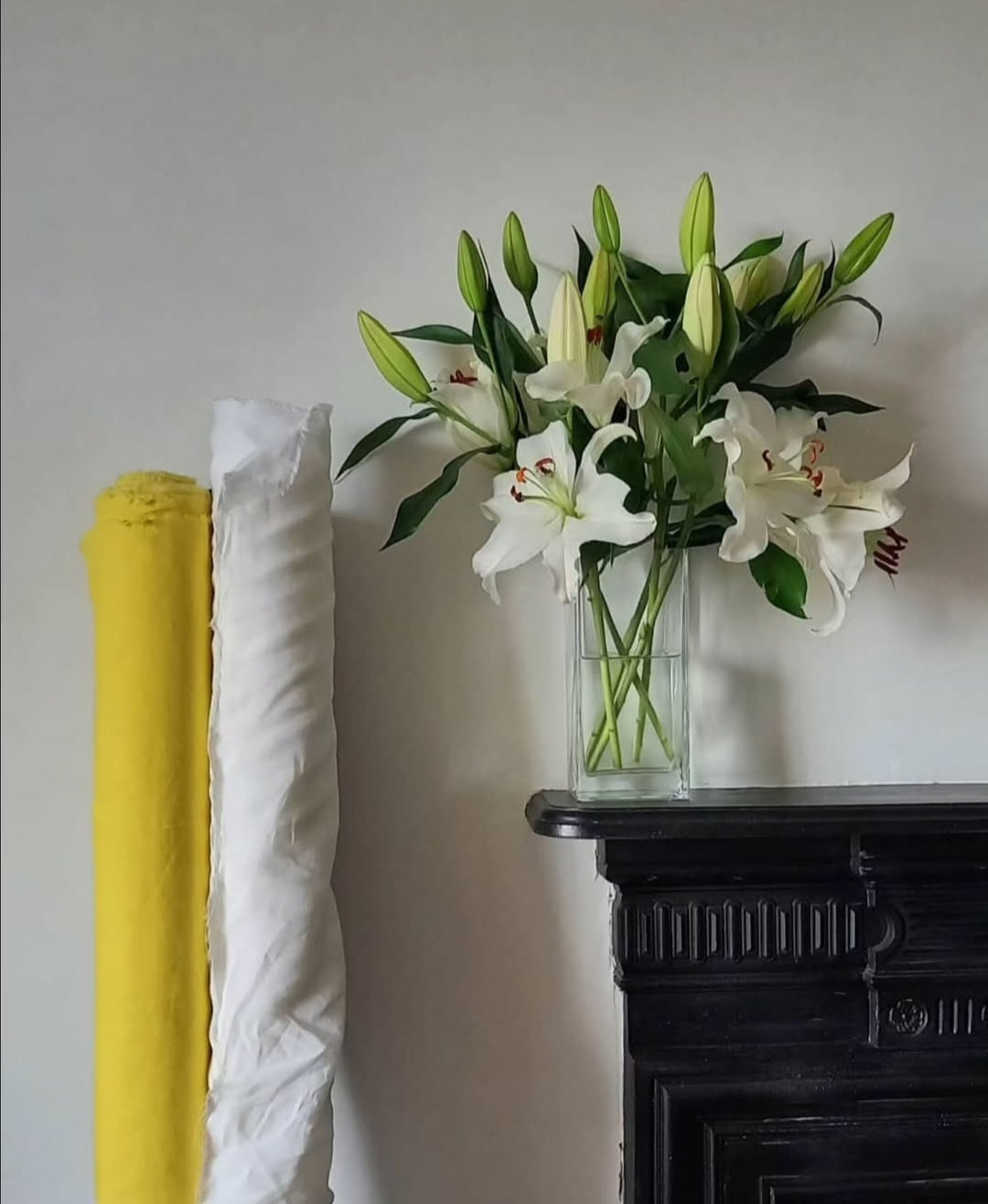 Rolls of 100% pure Irish linen beside white lilies in natural light within The Costume Room studio.