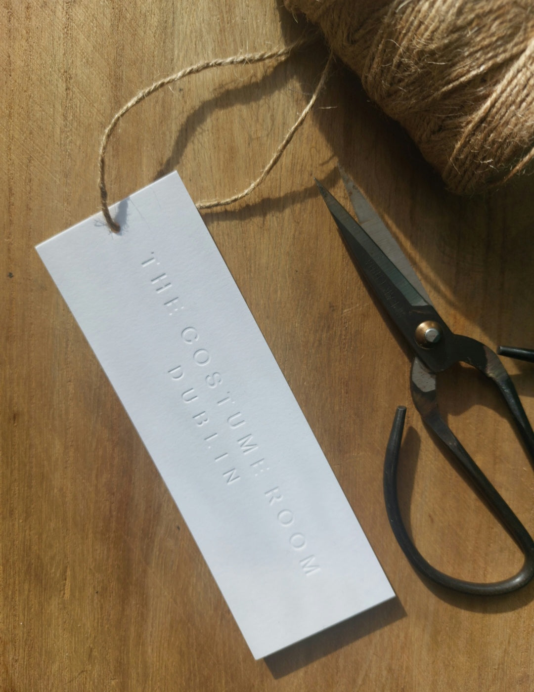 The Costume Room Dublin letterpress swing tag beside scissors and twine in natural light.