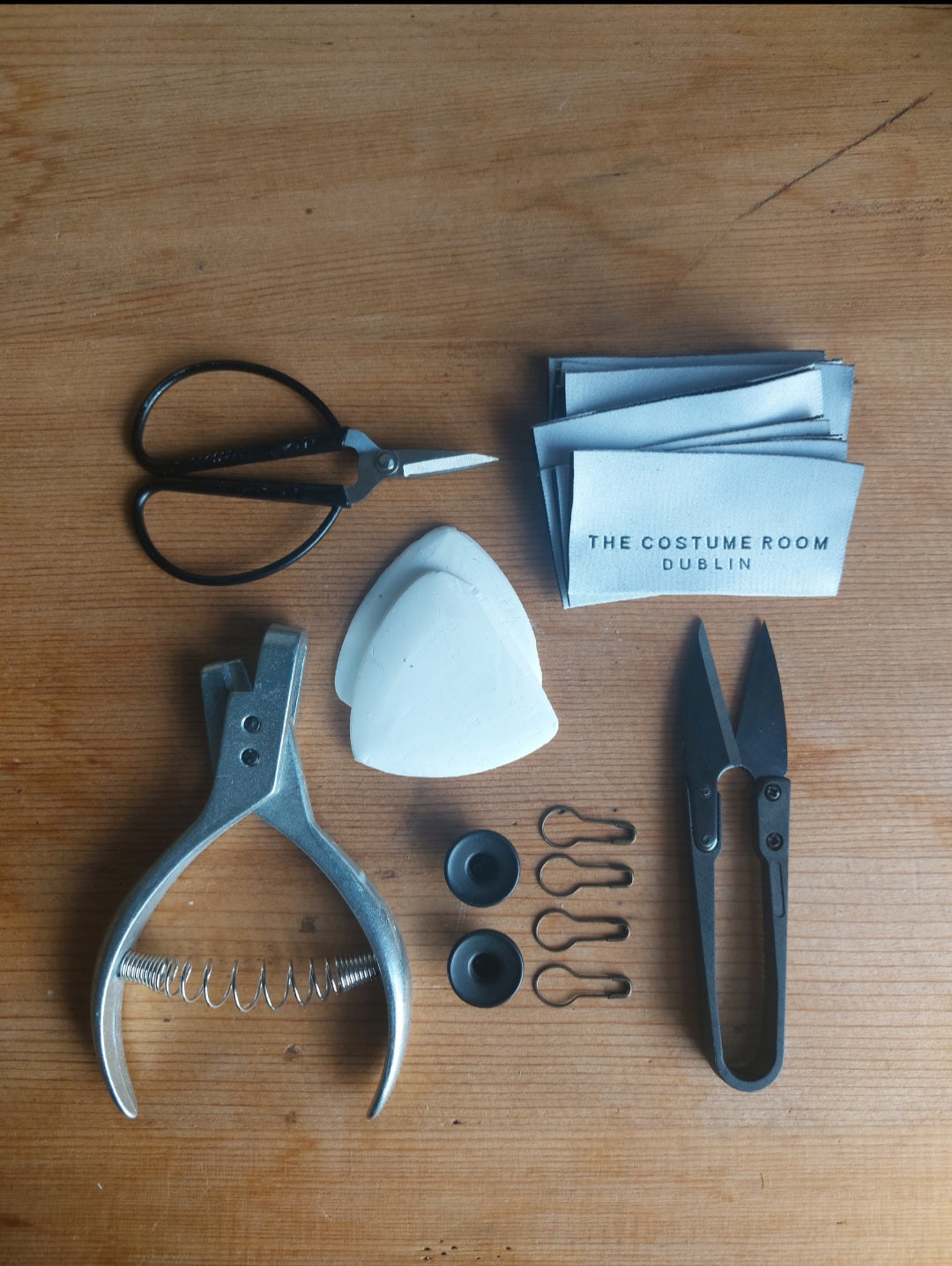 Studio tools and The Costume Room woven labels arranged on a wooden worktable in the Dublin studio.