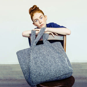 Woman wearing The Costume Room monochrome herringbone Handwoven Donegal Tweed Bag on a chair