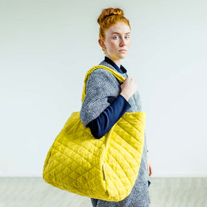 Woman wearing The Costume Room herringbone Handwoven Donegal Tweed Coat and yellow Linen Quilted Bag