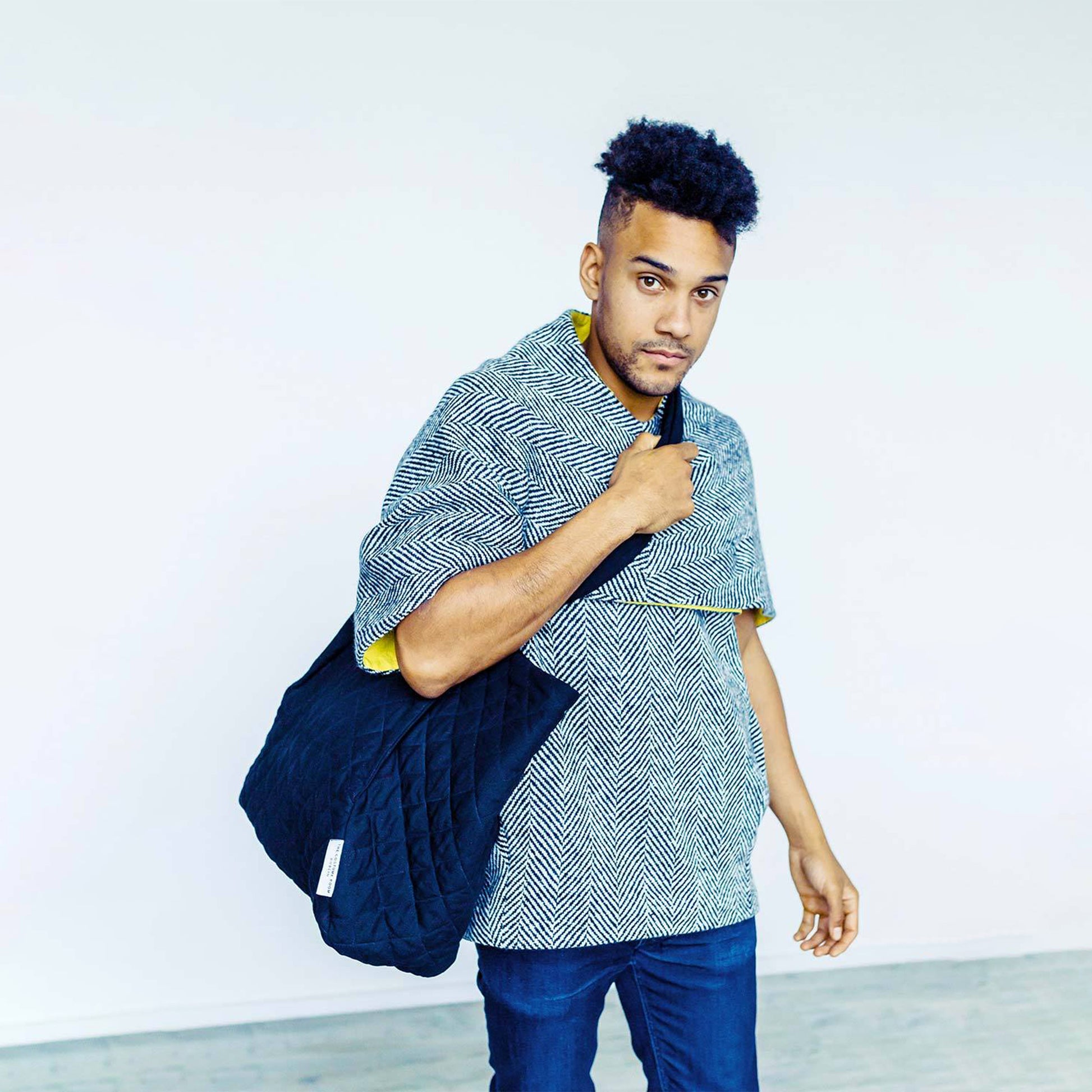 Man wearing The Costume Room Handwoven Donegal Tweed Top and Black Linen Quilted Crossbody Bag