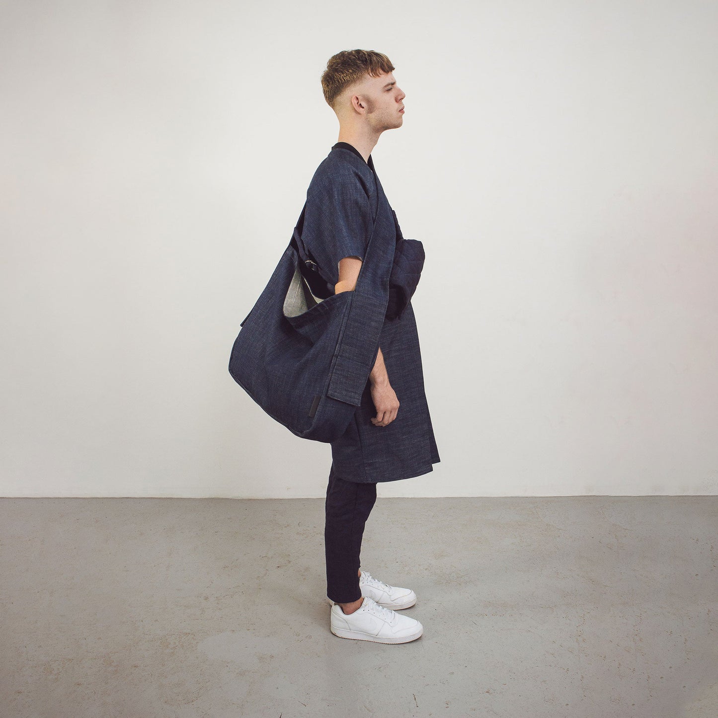 Man wearing The Costume Room Raw Organic Denim Crossbody bag and Raw Organic Denim Cocoon Long Jacket