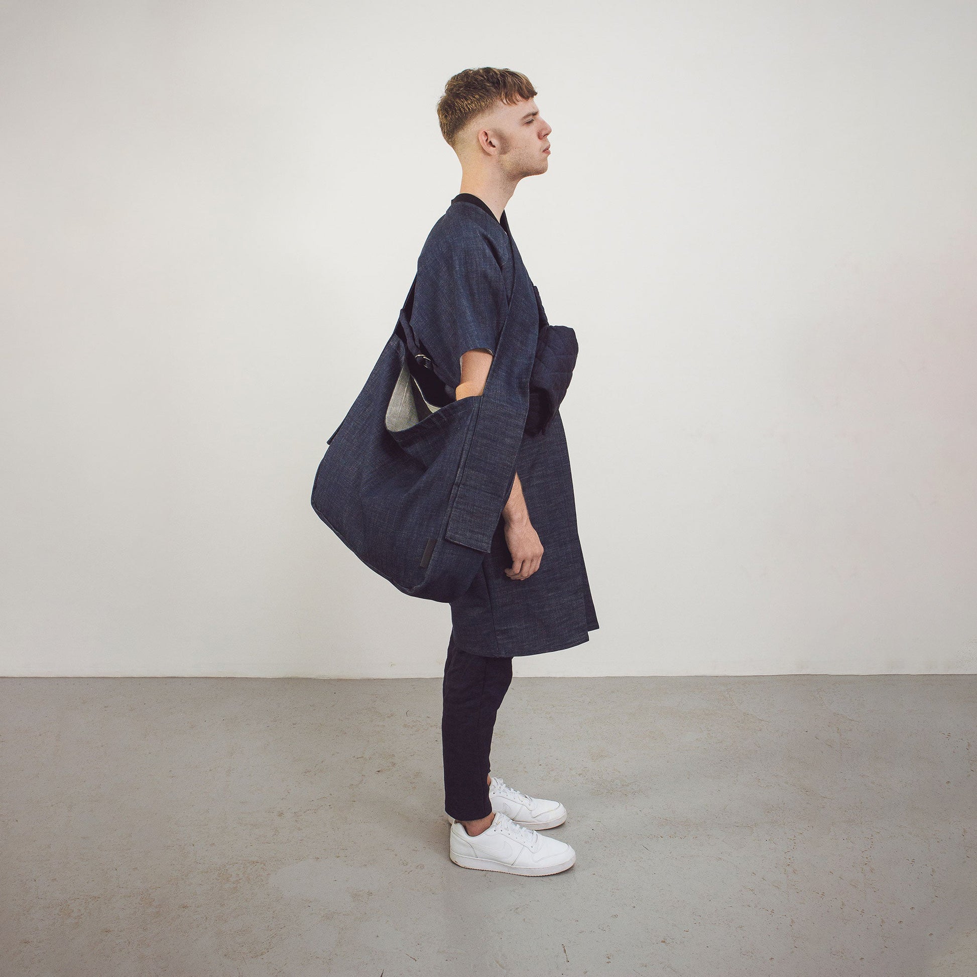 Man wearing The Costume Room Raw Organic Denim Crossbody bag and Raw Organic Denim Cocoon Long Jacket