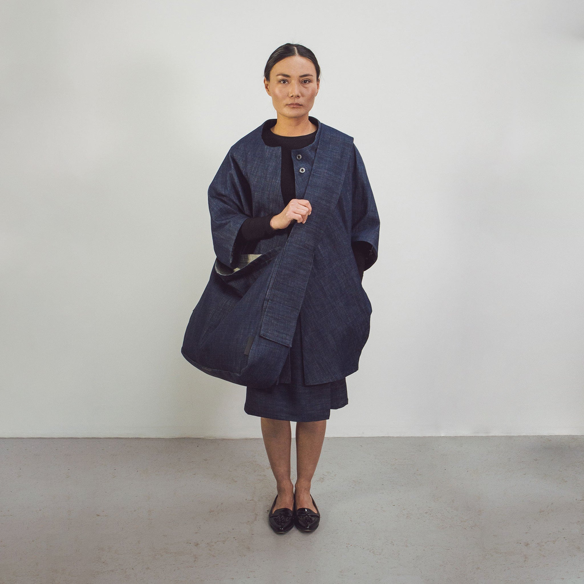 Woman wearing Raw Organic Denim Crossbody bag styled with Raw Organic Denim cocoon coat by The Costume Room